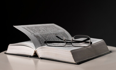 Wall Mural - Eyeglasses and open book on black background. Education and wisdom concept