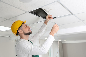 Wall Mural - Electrician in uniform repairing ceiling wiring indoors