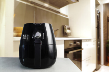 a black deep fryer or oil free fryer , air fryer appliance, is on the white marble table in the nice interior design kitchen of the house during the cooking dinner for family member in Christmas party