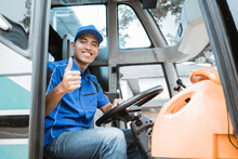 A Male Driver In Uniform Smiles At The Camera With Thumbs Up While Sitting Behind The Wheel On The Bus