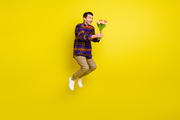 Full length profile side photo of young handsome man happy smile jump hold flowers bouquet isolated over yellow color background