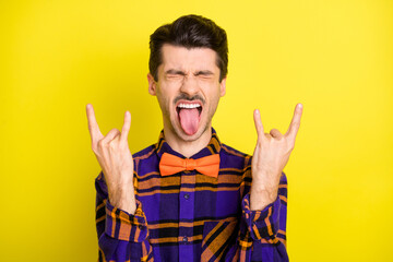 Poster - Photo of young brutal careless man crazy grimace tongue-out show rock sign isolated over yellow color background