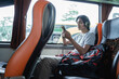 a man wearing headphones while listening music from a handphone while sitting by the window on a bus trip