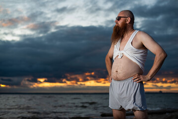 Wall Mural - Humorous portrait of a brutal man posing on the beach at sunset