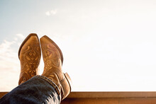 Cowboy Resting Legs With Feet Crossed - Sky Background - Negative Space - Boots And Jeans