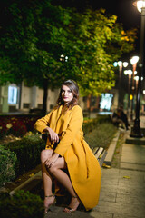 Canvas Print - Beautiful and elegant Caucasian woman in a black dress and a yellow coat posing on a street at night