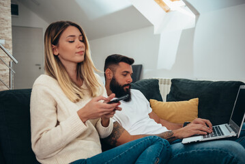 Wall Mural - Couple using a smartphone and a laptop at home