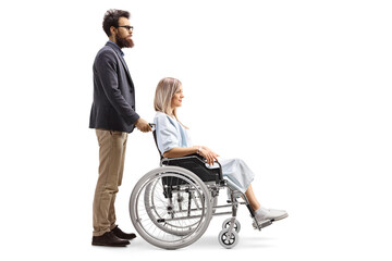 Wall Mural - Full length profile shot of a bearded man pushing a young woman patient in a wheelchair