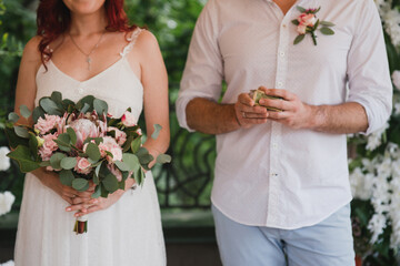 Love on wedding day. Closeup of bride and groom hold a bridal bouquet in their hands and showing their rings of newlyweds.