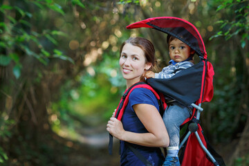 Mother with toddler child in backpack carrier is hiking in forest