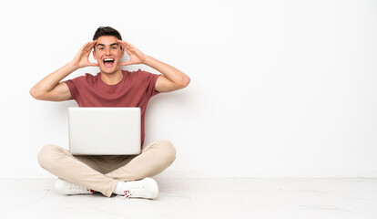 Wall Mural - Teenager man sitting on the flor with his laptop with surprise expression