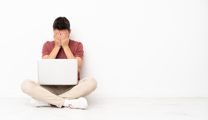 Teenager man sitting on the flor with his laptop with tired and sick expression
