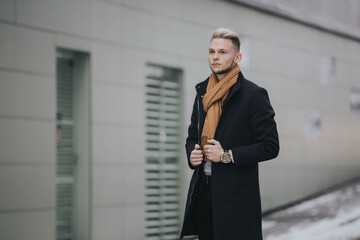 Wall Mural - Vertical shot of a Caucasian fashionable  man with a brown scarf on the wall background