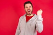 © Roquillo - Young caucasian man wearing tracksuit over red background angry and mad raising fist frustrated and furious while shouting with anger. Rage and aggressive concept.