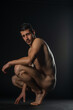 © qunica.com - Portrait of a naked male model posing squatted on black studio background