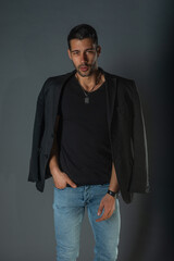 Handsome fashionable model in a black t-shirt with a jacket on his shoulders posing in a studio