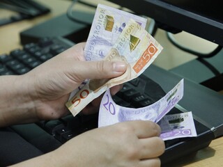 hands of a woman counting Swedish money on a computer keyboard