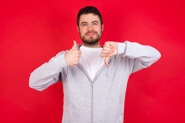 young handsome caucasian man in sports clothes against red background showing thumb up down sign