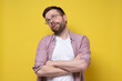 © koldunova - Caucasian man in glasses and casual clothes looks up distantly with arms crossed, he is bored and uninteresting. Yellow background.