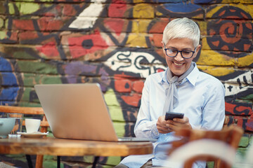 Wall Mural - An elderly woman using a smartphone while spending free time at bar's garden. Leisure, bar, friendship, outdoor