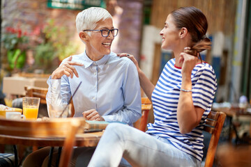 Wall Mural - Two female friends of different generations have a friendly talk while they have a drink in the bar. Leisure, bar, friendship, outdoor