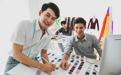 Cheerful Asian tailors inspecting sketch together