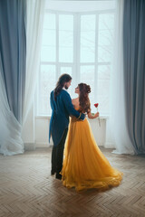 Happy couple embrace in white room old castle near window. Happy beauty sexy woman fantasy princess in yellow dress and man prince. Romantic male king hugs girl. Art Vintage style costume rear view.