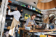 © sofiko14 - Two multicultural workers in uniform doing inventory together at decor shop. Bearded caucasian man using laptop while african woman counting goods.