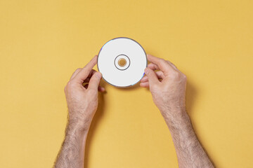 Sticker - Top view of male hands holding a blank CD-DVD mockup in front of yellow background