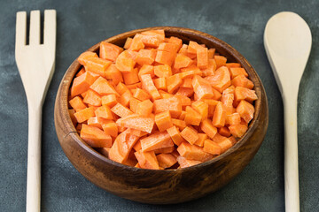 Fresh diced carrots in old wooden plate. On table is fork and spoon. Farm natural products. Healthy eating. Vegan menu