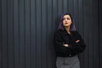 Wall Mural - Cool European female with purple hair leaning on a black fence