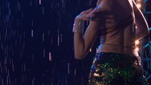 Sexy Oriental Dancer Enjoys Belly Dancing Under The Raindrops In A Dark Studio With Blue Lights. Close Up Of Flexible Young Woman Body With Long Dark Hair In Shiny Suit. Slow Motion.