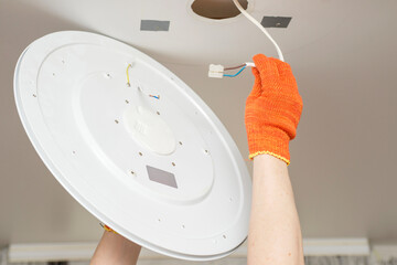 An electrician installs a chandelier on the ceiling. Hands of an electrician are installing and connecting a lamp to a ceiling. Ceiling lamp repair