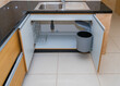 Closeup of the opened kitchen sink cabinet with a plastic trashcan