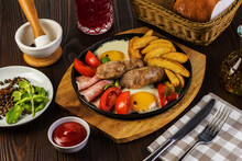 Fried Sausages With With Bacon And Fried Eggs And Fried Potatoes On A Rustic Background