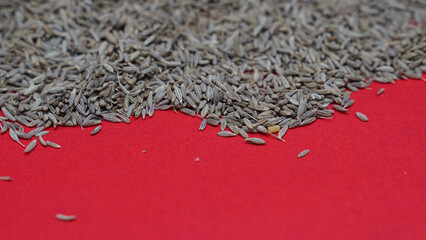 Sticker - Closeup of a pile of dry cumin seeds on the red surface - space for text