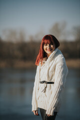 Poster - Vertical shot of a young smiling female with red hair posing in a warm white sweater