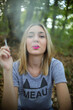 Vertical shot of a young blonde female smoking sitting on the ground in the forest