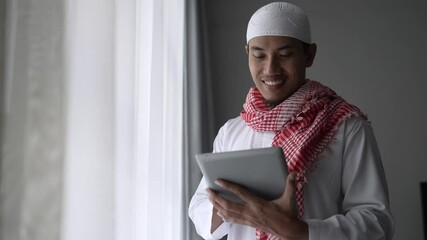 Wall Mural - happy muslim businessman smiling while using tablet pc near window