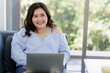 © Bangkok Click Studio - Asian young happy beautiful plus size sexy fat chubby smart female model sit relaxing on sofa smiling look at camera using laptop computer work from home in quarantine time from covid pandemic moment