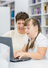 Poster - Young girl with down syndrome  uses a laptop with her teacher at library. Education for disabled children concept