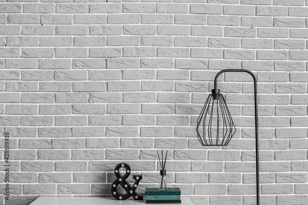 Table with decor and lamp near brick wall in room