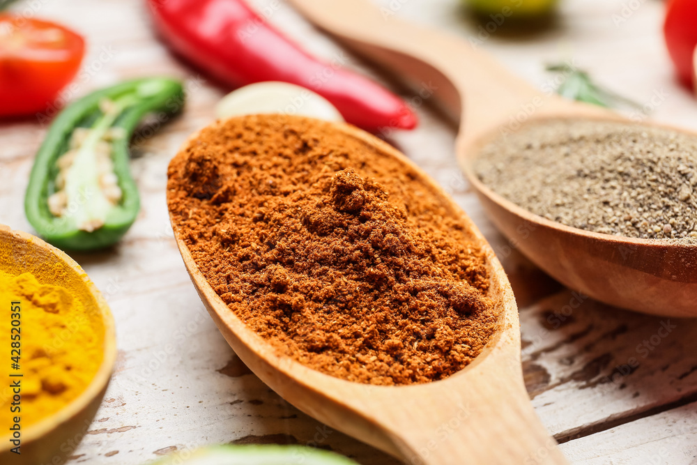 Spoons with different spices on light wooden background, closeup