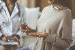 © rogerphoto - Close-up woman-patient holding pills near her doctor, time to take medications, cure for headache or remedy pain killer drugs. Stay at home concept during Coronavirus pandemic and self isolation