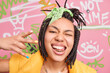 © wayhome.studio - Trendy cheerful hipster girl makes yo gesture shows golden teeth and tongue winks eye enjoys cool modern music stands near graffiti wall enjoys her freedom. Stylish female rapper in urban place