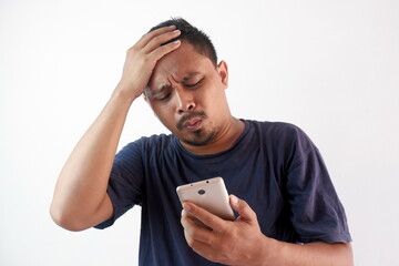 Wall Mural - man upset holding phone with hand on forehead, stressed guy looking smartphone screen, unhappy broke man