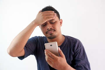 Wall Mural - upset man holding phone with hand on forehead, stressed guy looking smartphone screen