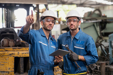 Wall Mural - Mechanic holding a wrench and a tablet standing in front of an industrial forklift. Professional technicians are holding a tablet to control work in industrial plants.