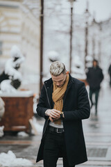 Canvas Print - Handsome young man in a black winter outfit with a brown scarf checking his watch while walking