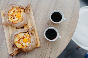 Two khachapuri and two cups of coffee, a dish of georgian cuisine on a wood table in an office